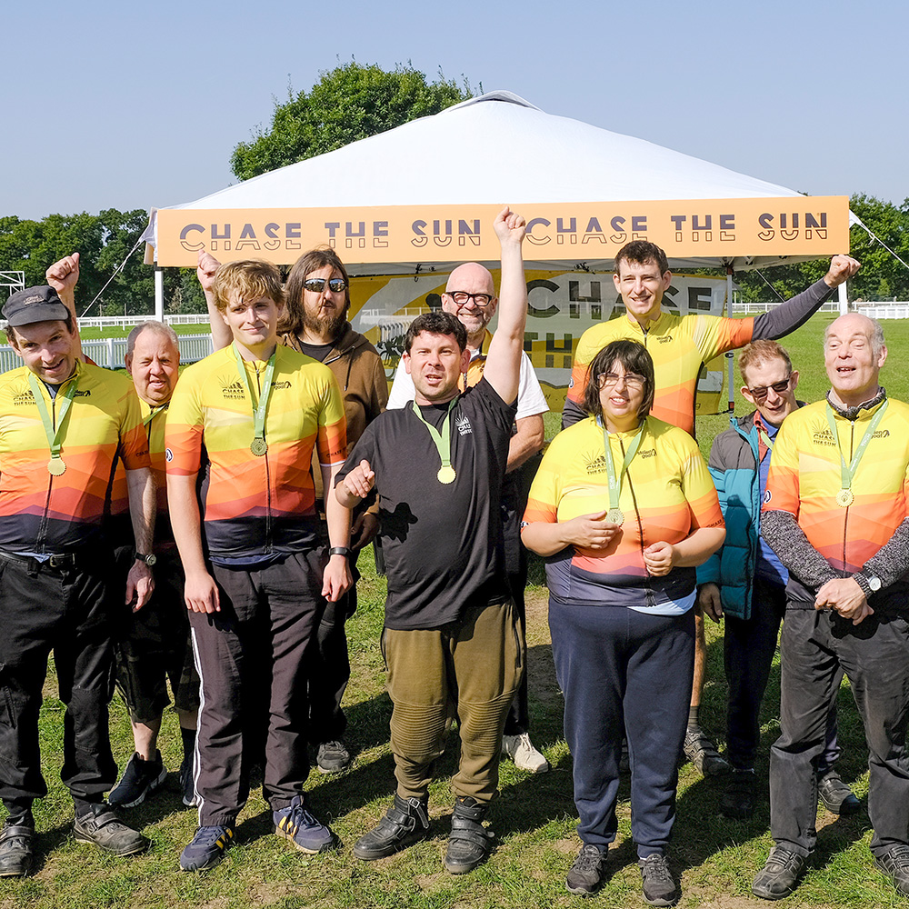 A group of cyclists cheering with medals in front of a Chase the Sun gazebo