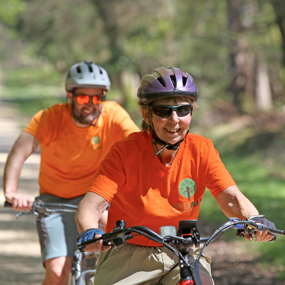 Two PEDALL volunteers on bikes smiling as they cycle through the New Forest