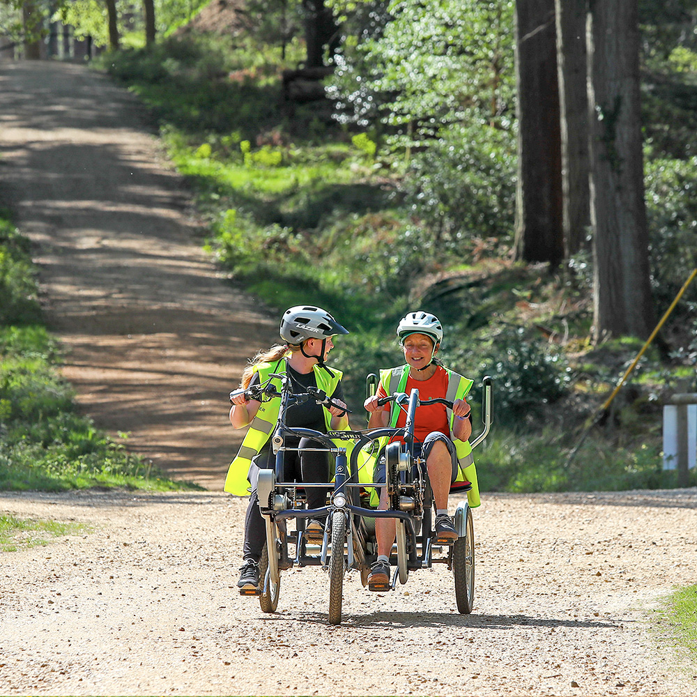 Two smiling cyclists on a tandem bike going along a gravel path in the New Forest
