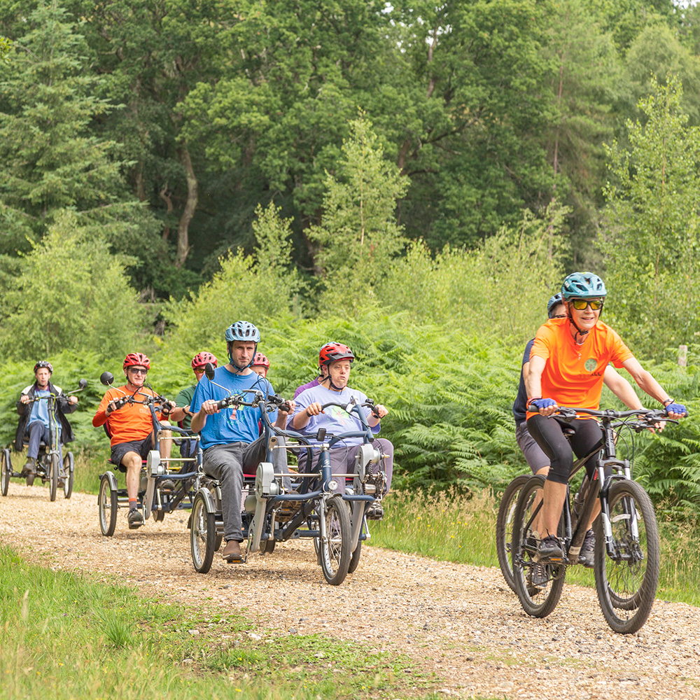 A group of cyclists on a variety of adaptive bikes led by a PEDALL volunteer along a cycle path in the New Forest, Hampshire